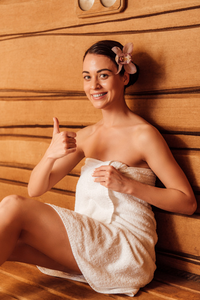 Lächelnde Frau im Handtuch zeigt Daumen nach oben in der Sauna - Foto, Bild