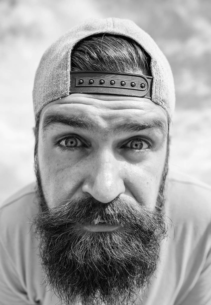 Looking so closely. Serious hipster in street fashion wear on cloudy sky. Brutal man with long beard and mustache. Bearded man in fashion hipster cap outdoor. Cool hipster - Foto, Bild