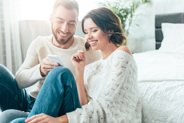 cheerful man holding smartphone near happy brunette woman at home  - Photo, Image