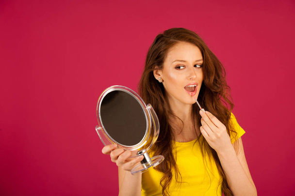 attractive young woman applying lip gloss looking in mirror over - Фото, зображення