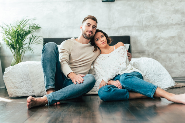 handsome man hugging attractive woman while sitting on floor and watching movie at home - Foto, Bild