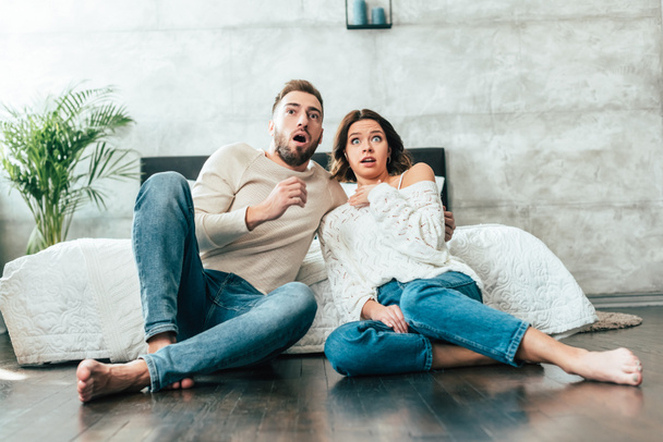 shocked man and woman sitting on floor and watching movie at home  - Φωτογραφία, εικόνα