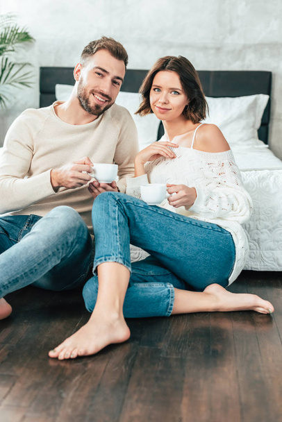 handsome man and beautiful woman sitting on floor and holding cups with drinks - Foto, immagini