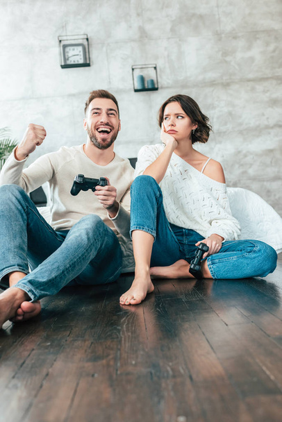 low angle view of upset woman looking at happy man gesturing while playing video game  - Foto, afbeelding