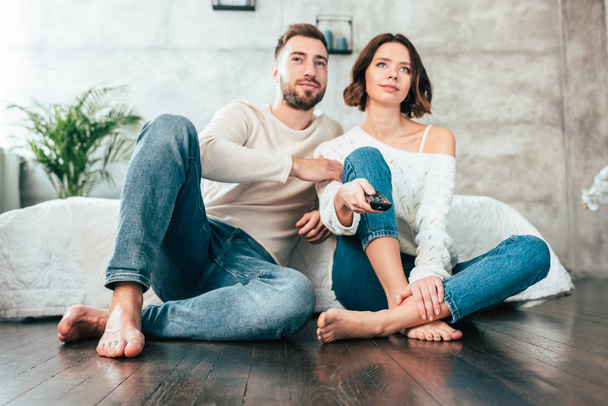 low angle view of happy man sitting on floor near attractive woman with remote controller  - Фото, изображение