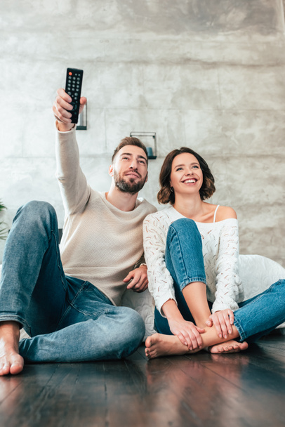 low angle view of handsome man sitting on floor near happy woman and holding remote controller  - Foto, imagen