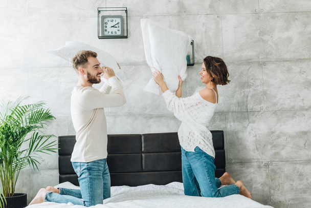 happy man having pillow fight with attractive woman on bed  - Fotografie, Obrázek