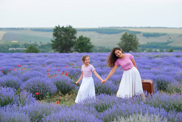 joven mujer y niña están caminando a través del campo de flores de lavanda, hermoso paisaje de verano
 - Foto, imagen