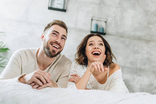 low angle view of happy man near smiling brunette woman pointing with finger bedroom  - Fotó, kép