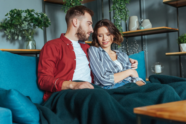happy man looking at brunette woman while sitting on sofa at home  - Фото, зображення