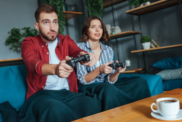 selective focus of handsome man and brunette woman playing video game in living room  - Фото, изображение