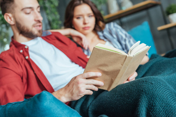 selective focus of man reading book near brunette woman at home  - Fotografie, Obrázek
