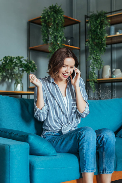 cheerful woman gesturing while talking on smartphone in living room  - Foto, Imagem