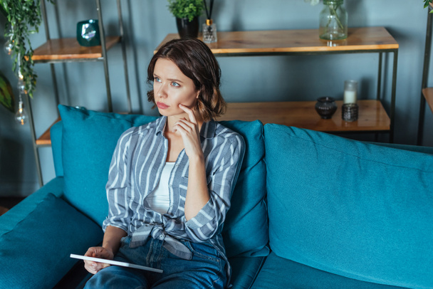 overhead view of pensive brunette woman holding digital tablet while sitting in living room  - Φωτογραφία, εικόνα