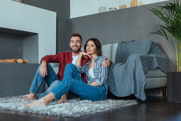 happy man smiling while sitting on carpet with beautiful brunette woman  - Zdjęcie, obraz