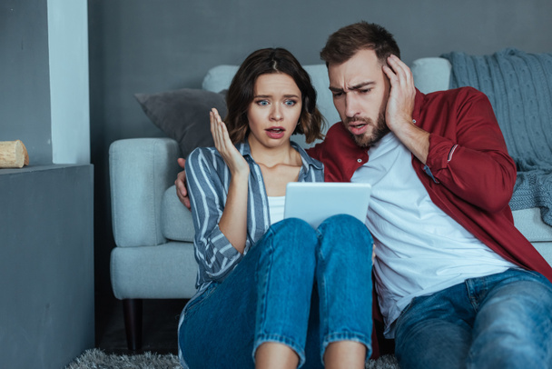 shocked man and woman gesturing while watching video on digital tablet  - Fotó, kép