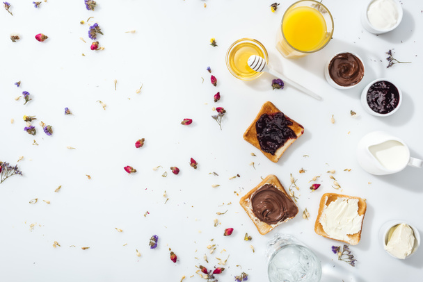 Blick von oben auf leckere Toasts mit Marmelade, Schokocreme und Frischkäse in der Nähe von Gläsern mit Orangensaft und Wasser auf weiß  - Foto, Bild