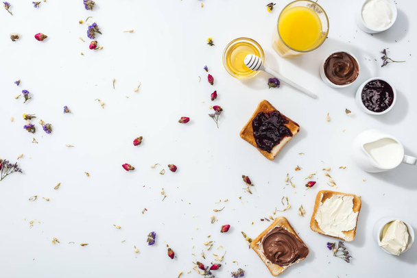 top view of tasty toasts with jam, chocolate cream and cream cheese near honey and glass of orange juice on white  - Foto, Bild
