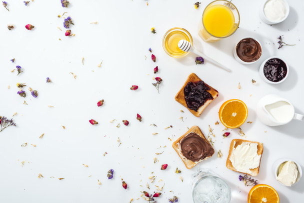 top view of tasty toasts, bowls with jam and oranges near glasses of water and orange juice on white - Fotografie, Obrázek