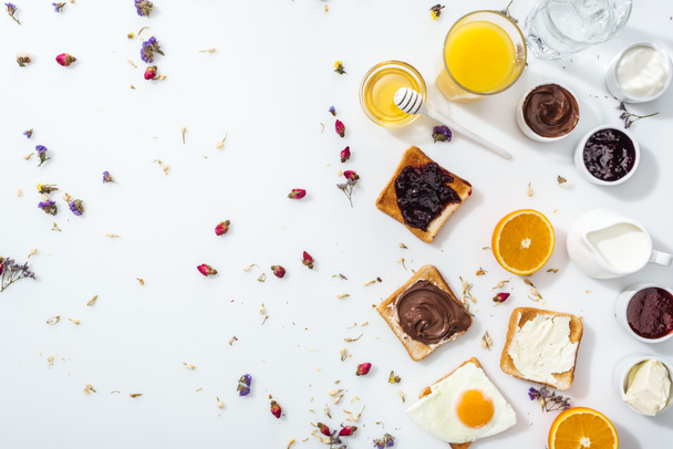 top view of toasts, jam and fried egg near glasses of water and orange juice on white - Fotoğraf, Görsel