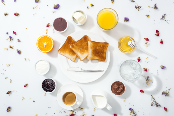 Teller mit Toasts in der Nähe von Schüsseln mit Marmelade, Honig, Schokoladencreme und Frischkäse in der Nähe von Gläsern auf weiß  - Foto, Bild