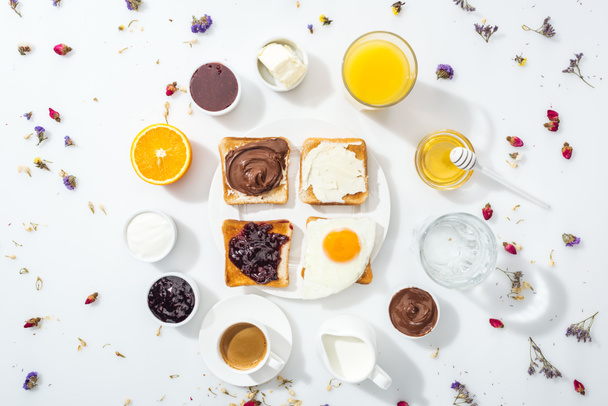 top view of tasty toasts with jam, cream cheese, chocolate cream and friend egg near drinks on white  - Foto, Imagem