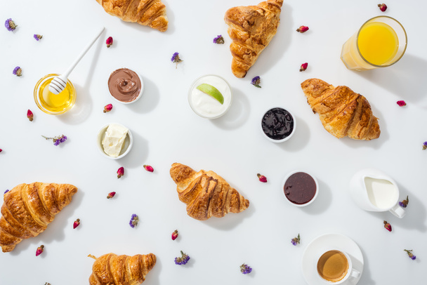 top view of croissants near bowls with jam, honey, orange juice and dried flowers on white  - Photo, Image