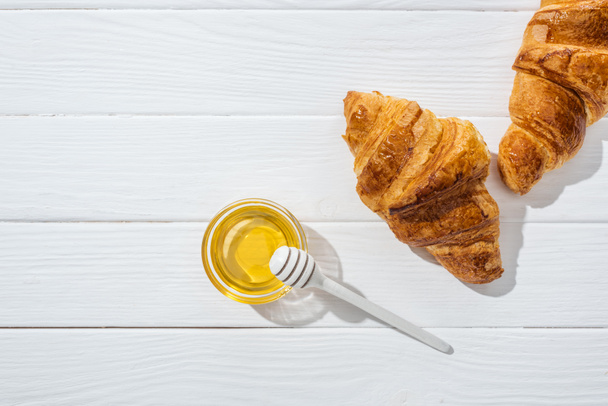 ylhäältä näkymä maukkaita ja tuoreita croissanteja lähellä lasi kulho hunaja ja hunaja dipper valkoisella pinnalla
  - Valokuva, kuva