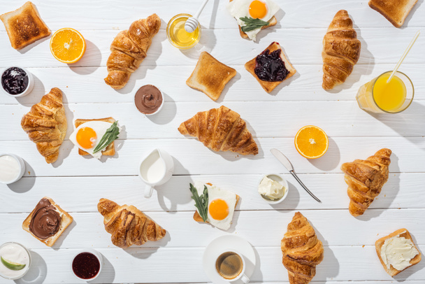 top view of sweet croissants near tasty toasts with jam and fried eggs on white  - Photo, Image