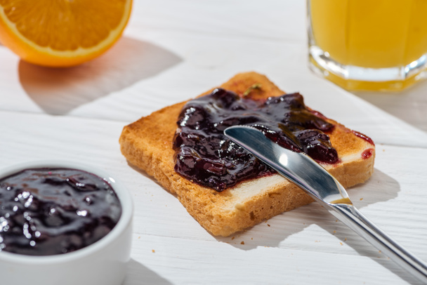 selektiver Toastfokus mit Marmelade in Messernähe und einer Hälfte Orange auf Weiß  - Foto, Bild