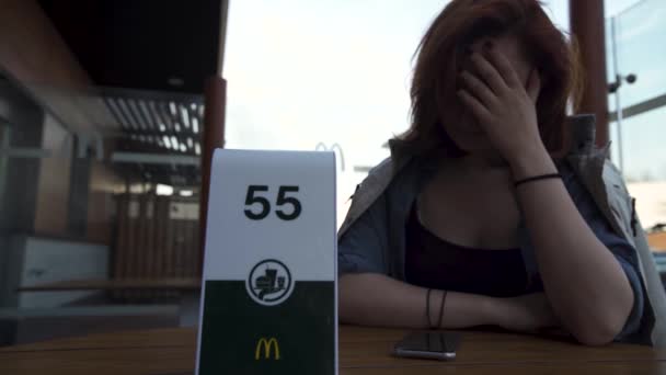 RIGA, LATVIA - APRIL 22, 2019: Waiting for order and thinking about her weight - Young Woman eating in Fast Food Restaurant Mcdonalds - Кадры, видео