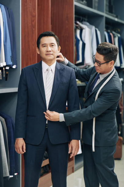 Erkek giyim mağazası asistanı orta yaşlı Vietnamlı adam mükemmel takım seçmek için yardım - Fotoğraf, Görsel