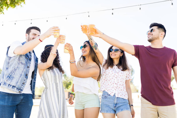 Unbekümmerte junge Männer und Frauen stoßen beim Sommerfest im Freien auf Biergläser an - Foto, Bild