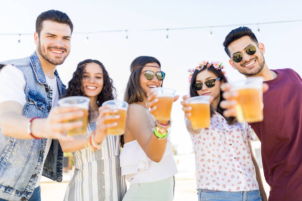 Portrait of fun loving friends holding beer glasses at music festival - Foto, Imagen