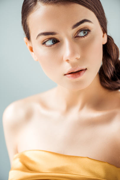 dreamy young woman with shiny lips and golden eye shadow looking away isolated on grey - Photo, Image