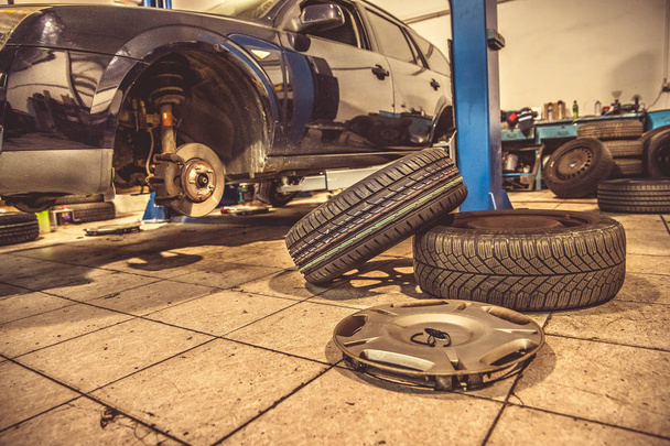 Substituindo pneus de inverno em pneus de verão em uma garagem profissional com a ajuda de ferramentas profissionais. carro em um macaco hidráulico
 - Foto, Imagem