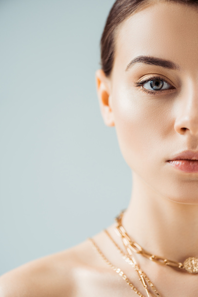 cropped view of young woman with shiny makeup in golden necklaces looking at camera isolated on grey - Fotoğraf, Görsel
