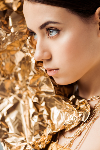 młoda kobieta z błyszczącym makijażem i złotą folią w naszyjnikach odwracając wzrok - Zdjęcie, obraz