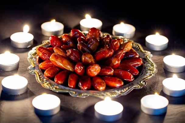 ramadan kareem concept mit getrockneten Datteln auf einem silbernen Tablett und vielen brennenden Kerzen ringsum. das muslimische Fest des heiligen Monats Ramadan Kareem Nacht Hintergrund. - Foto, Bild