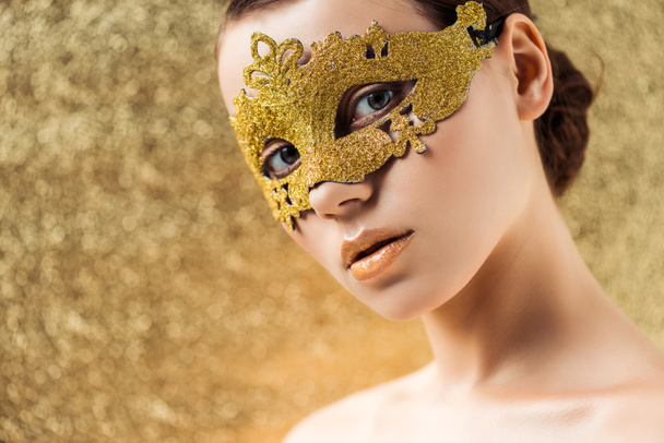 fiatal meztelen nő arany maszk fényes smink nézi kamera texturált arany háttér - Fotó, kép