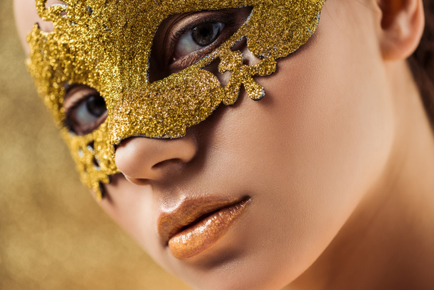vista de cerca de la mujer joven en máscara de oro con maquillaje brillante mirando a la cámara
 - Foto, Imagen