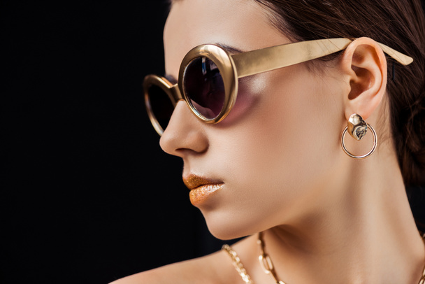 young nude woman in sunglasses, golden earring and necklaces isolated on black - Фото, зображення