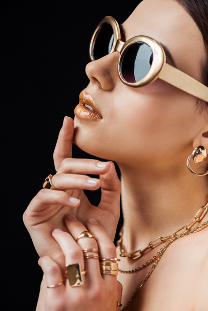 young nude woman in sunglasses, golden earring, rings and necklaces isolated on black - Foto, Imagen