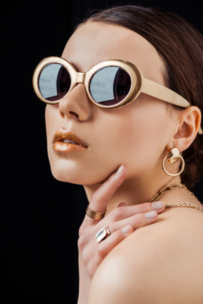 young naked woman in sunglasses and golden jewelry isolated on black - Fotografie, Obrázek