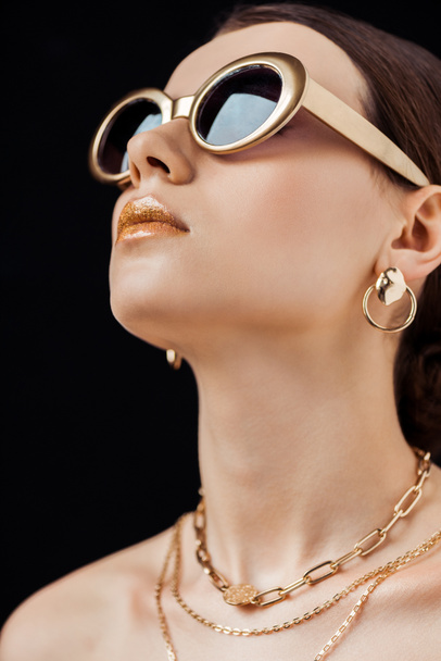 young attractive naked woman in sunglasses and golden jewelry isolated on black - Foto, Imagem