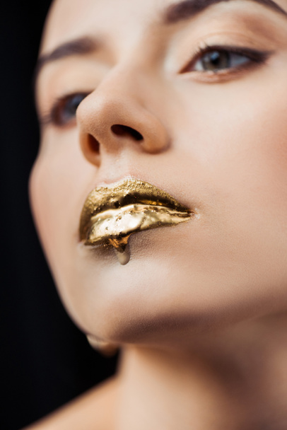 close up of young woman with golden painted lips isolated on black - Valokuva, kuva