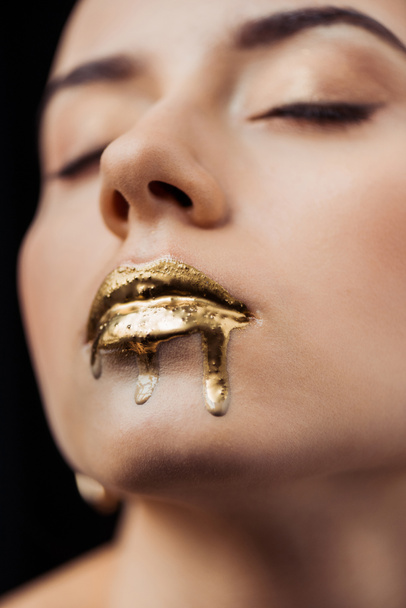 close up of young woman with closed eyes and golden painted lips isolated on black - Photo, Image