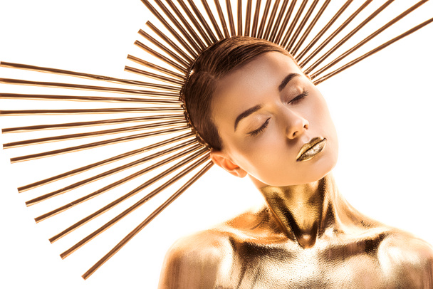 mujer joven desnuda pintada de oro con accesorio en la cabeza y ojos cerrados aislados en blanco
 - Foto, imagen