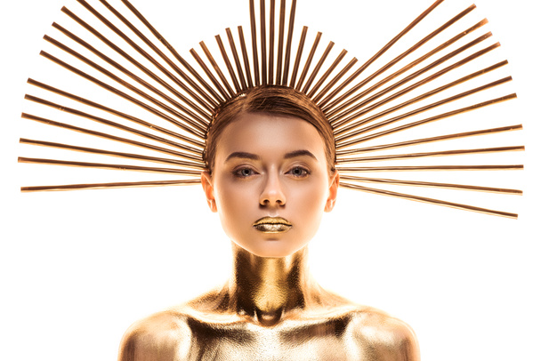 mujer joven desnuda pintada de oro con accesorio en la cabeza mirando a la cámara aislada en blanco
 - Foto, Imagen