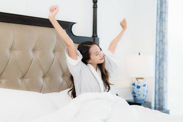 Retrato hermosa joven asiática mujer despierta con feliz relajarse y sonreír en la cama en el interior del dormitorio
 - Foto, Imagen